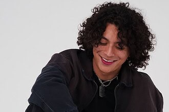 Frankie with curly hair smiling, celebrating new single "R0LL3RC0AST3R".